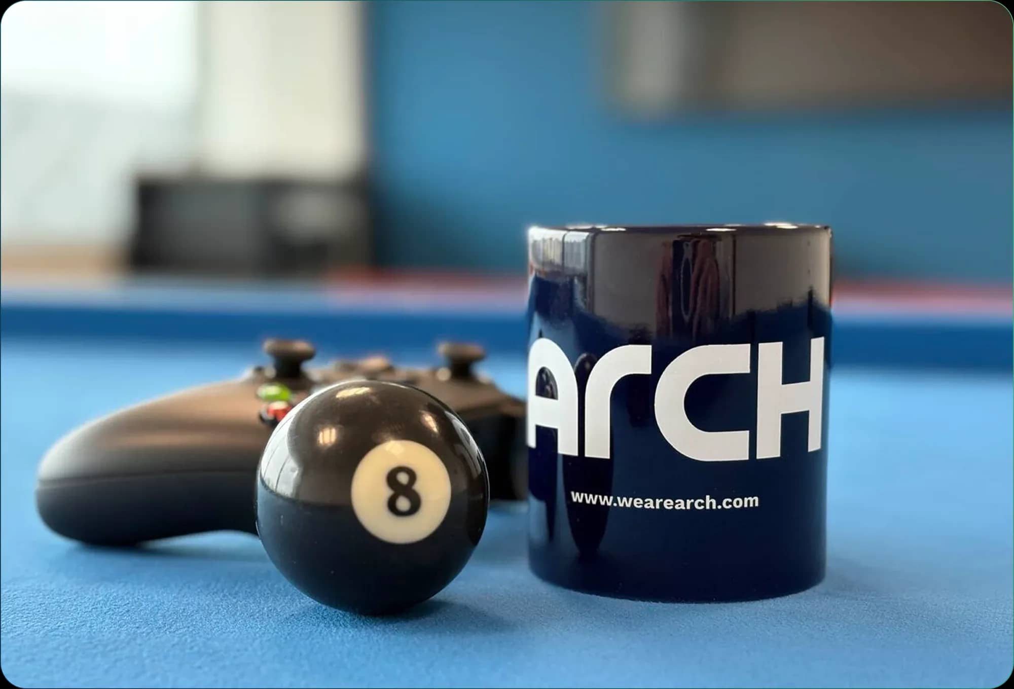 Arch mug, an 8 ball and a game controller on a blue pool table
